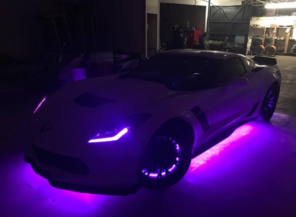 A dark garage with a white Corvette. It has purple DRLs and purple underbody kit.