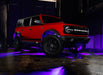 Three quarters view of a red Ford Bronco with rock lights glowing purple.