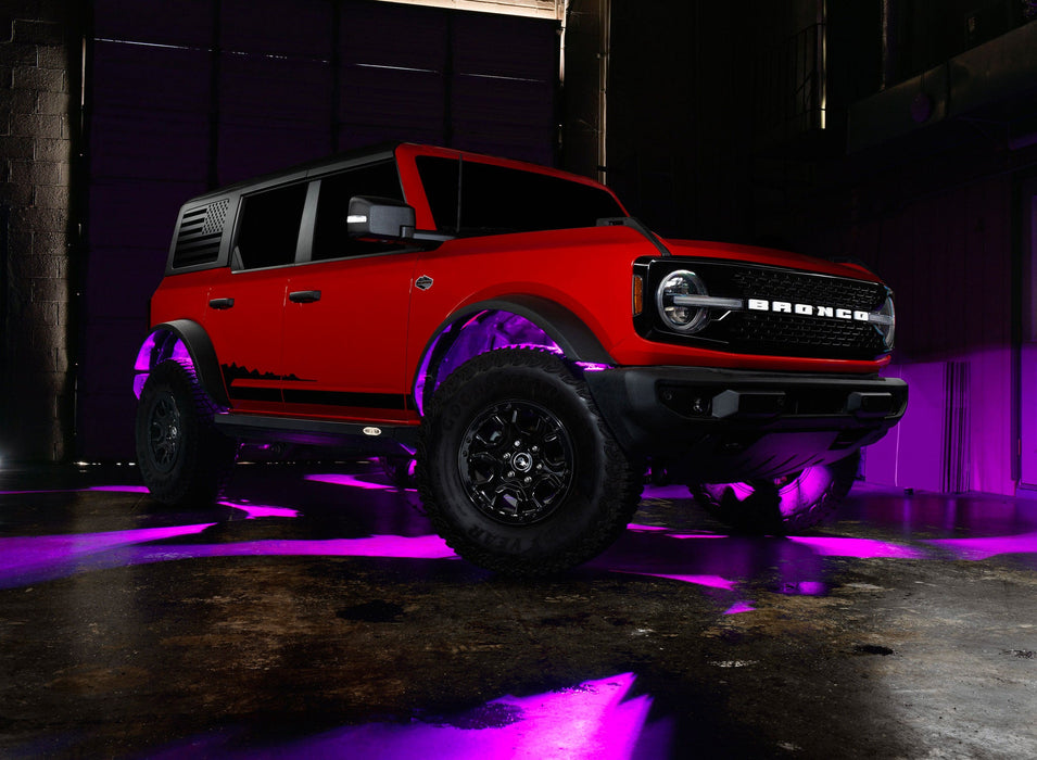 Three quarters view of a red Ford Bronco with rock lights glowing pink.