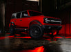 Three quarters view of a red Ford Bronco with rock lights glowing red.