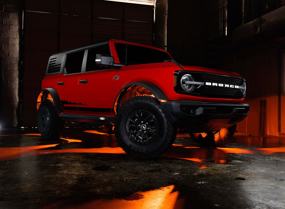 Three quarters view of a red Ford Bronco with rock lights glowing amber.