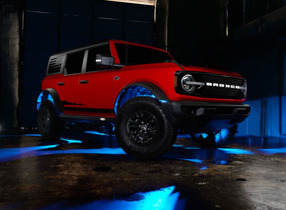Three quarters view of a red Ford Bronco with rock lights glowing cyan.
