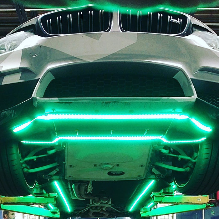 View from underneath a white BMW, showing LED underbody strips glowing green.