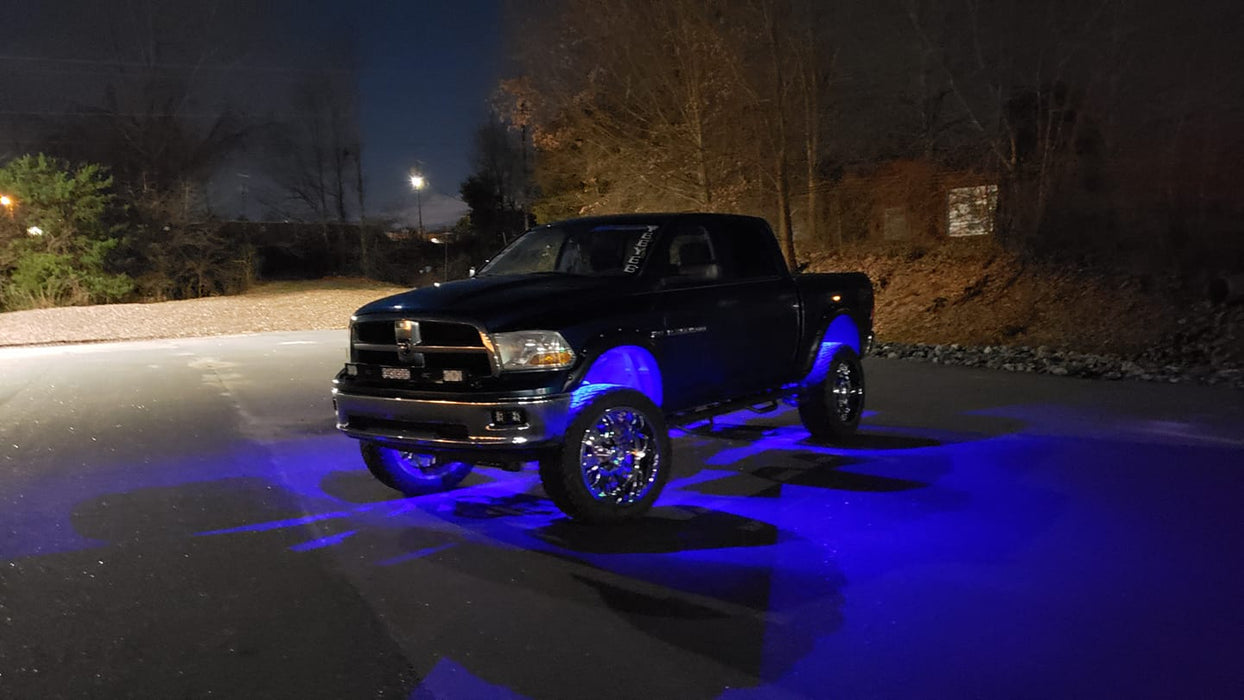Black truck in a parking lot with blue rock lights glowing.