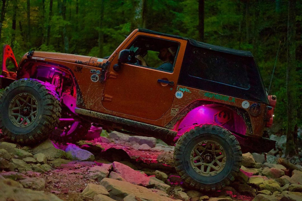 a Jeep driving on a rocky trail, with pink rock lights illuminating the trail.
