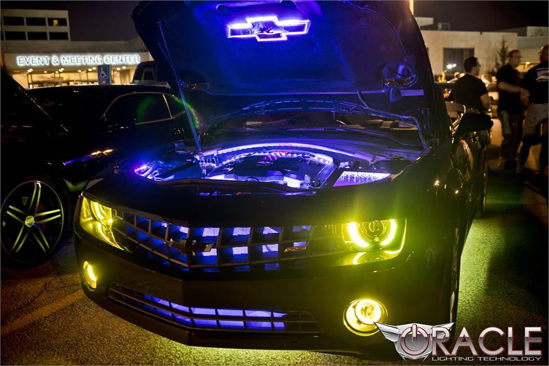 Camaro at a car show with blue engine bay lighting and yellow halo headlights.