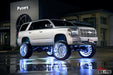 A silver lifted Chevrolet with white LED wheel rings installed, and the bright LEDs reflecting off the wet pavement.