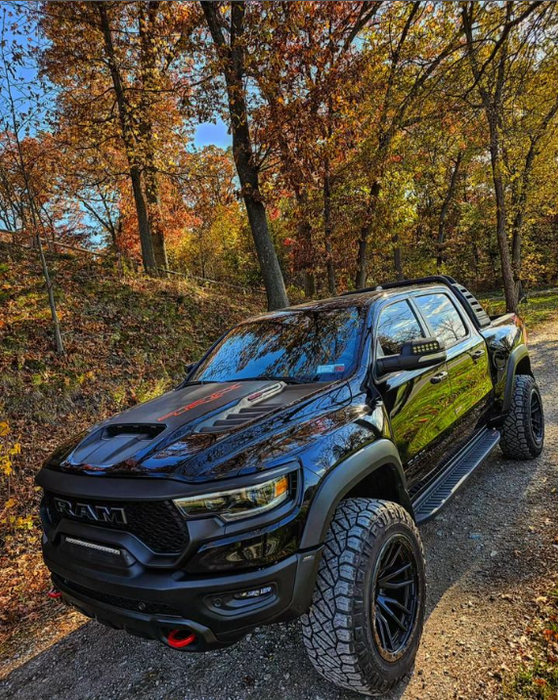 A black RAM TRX driving on a trail outdoors, with multiple ORACLE Lighting products installed, including LED Off-Road Side Mirror Ditch Lights, and Front Bumper Integrated Light Bar.