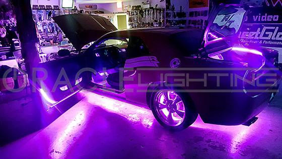 A Dodge Challenger in a garage with purple LED lighting on the car.