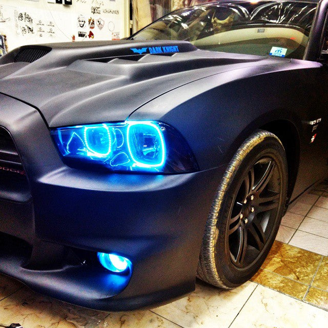 Close-up of cyan LED headlight halo rings installed on a black Dodge Charger.