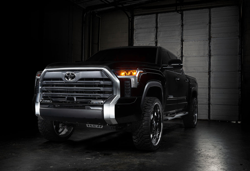 Three quarters view of a black Toyota Tundra with amber demon eye projectors.