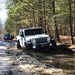 White Jeep Wrangler driving through a creek with Oculus Headlights turned on.