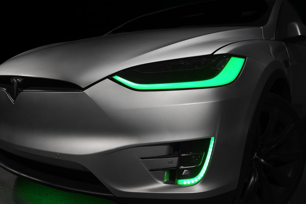 Close-up on the headlights and fog lights of a Tesla Model X with green DRLs.