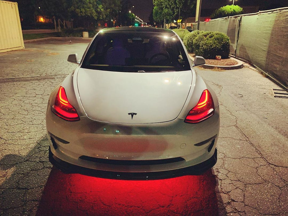 Straight front view of a Tesla Model 3 with red headlight DRLs.