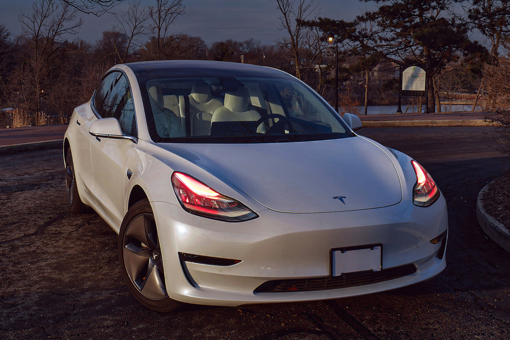 Three quarters view of a Tesla Model 3 with red headlight DRLs.