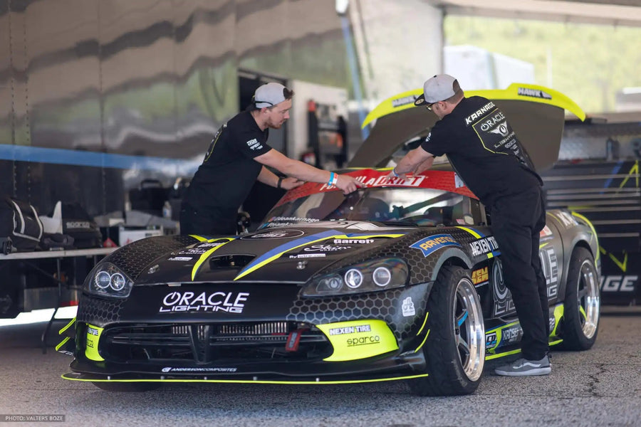 2 People working on a car, both wearing ORACLE Lighting Official Snap-Back Hat.