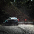 Front view of a black Dodge Challenger, with cyan LED headlight halo rings installed.