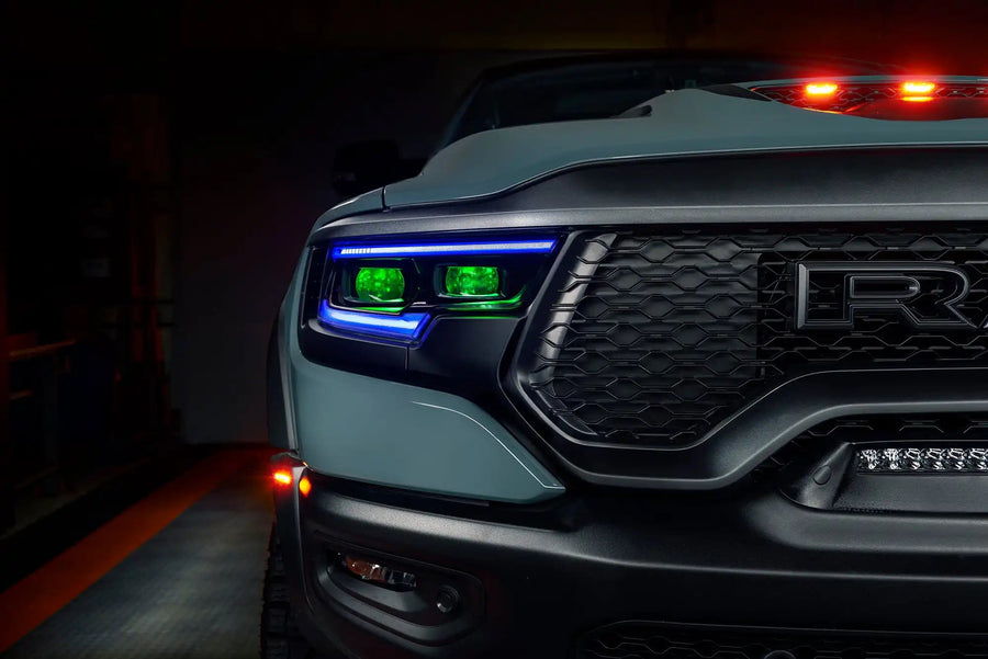 Close-up of Ram 1500 headlights with blue DRLs and green demon eye projectors.