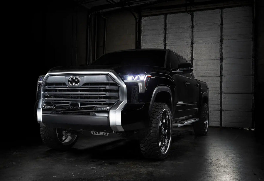 Three quarters view of a black Toyota Tundra with white demon eye projectors.