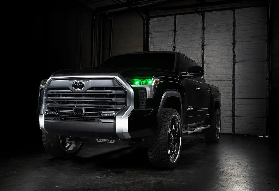 Three quarters view of a black Toyota Tundra with green demon eye projectors.