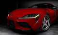 Close-up on the front end of a red Toyota Supra, with yellow headlight DRLs.