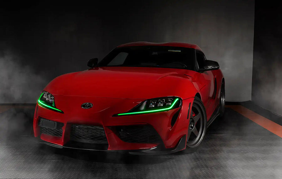 Three quarters view of a red Toyota Supra with green headlight DRLs.