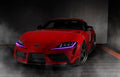 Three quarters view of a red Toyota Supra with pink headlight DRLs.