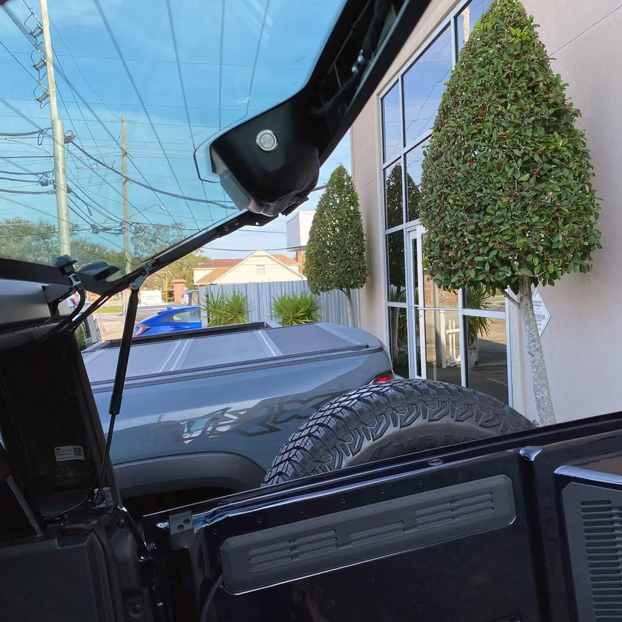 Car interior with open door and tire, reflected glass showing outdoor scene.
