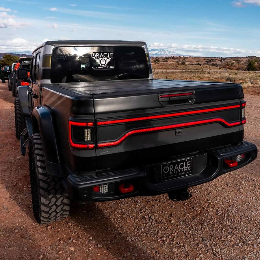 Rear end of a Jeep Gladiator JT with multiple ORACLE Lighting products installed. Including Racetrack LED Tailgate Panel, High Powered Reverse Lights, Flush Mount LED Tail Lights.