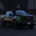 Three quarters view of a black GMC Sierra with green headlight DRLs.