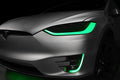 Close-up on the headlights and fog lights of a Tesla Model X with green DRLs.