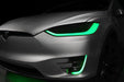 Close-up on the headlights and fog lights of a Tesla Model X with green DRLs.