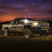 Dirtied pickup truck with headlights on in a field at sunset