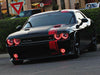 Three quarters view of a black Dodge Challenger with red LED headlight and fog light halo rings installed.