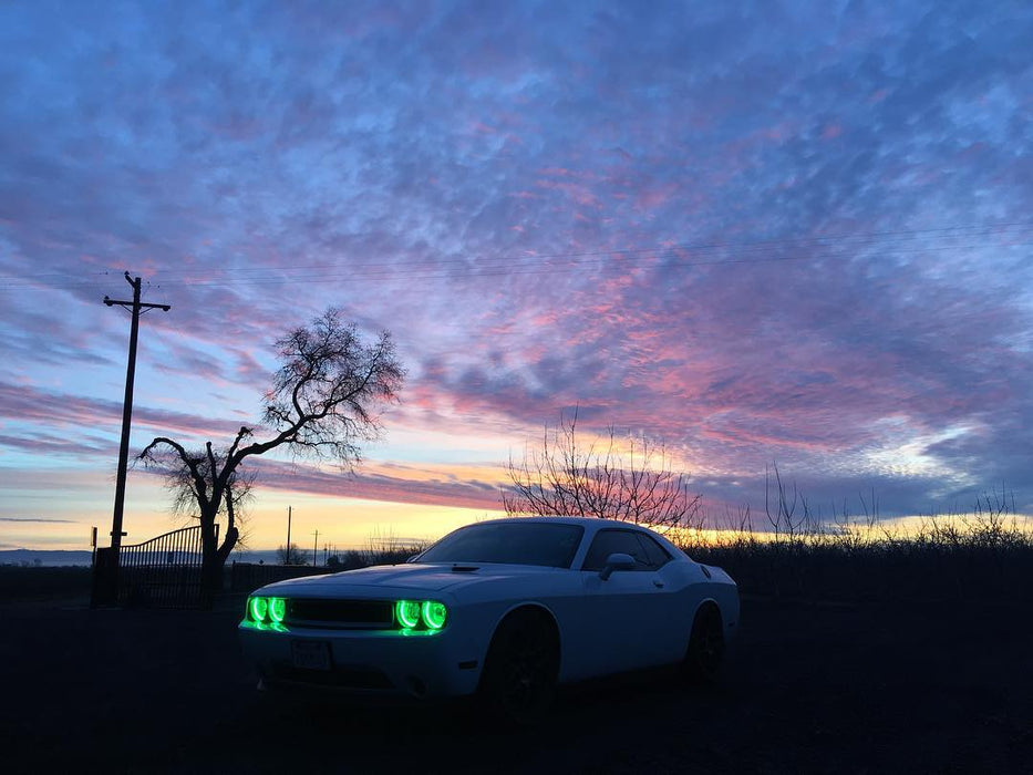 Three quarters view of a white Dodge Challenger with green LED headlight halo rings installed.
