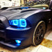 Close-up of cyan LED headlight halo rings installed on a black Dodge Charger.