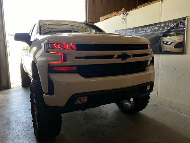 White Chevrolet Silverado with red demon eye projectors and DRLs.