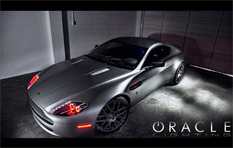 Three quarters view of an Aston Martin Vantage with red LED headlight halo rings installed.