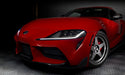 Close-up on the front end of a red Toyota Supra, with white headlight DRLs.