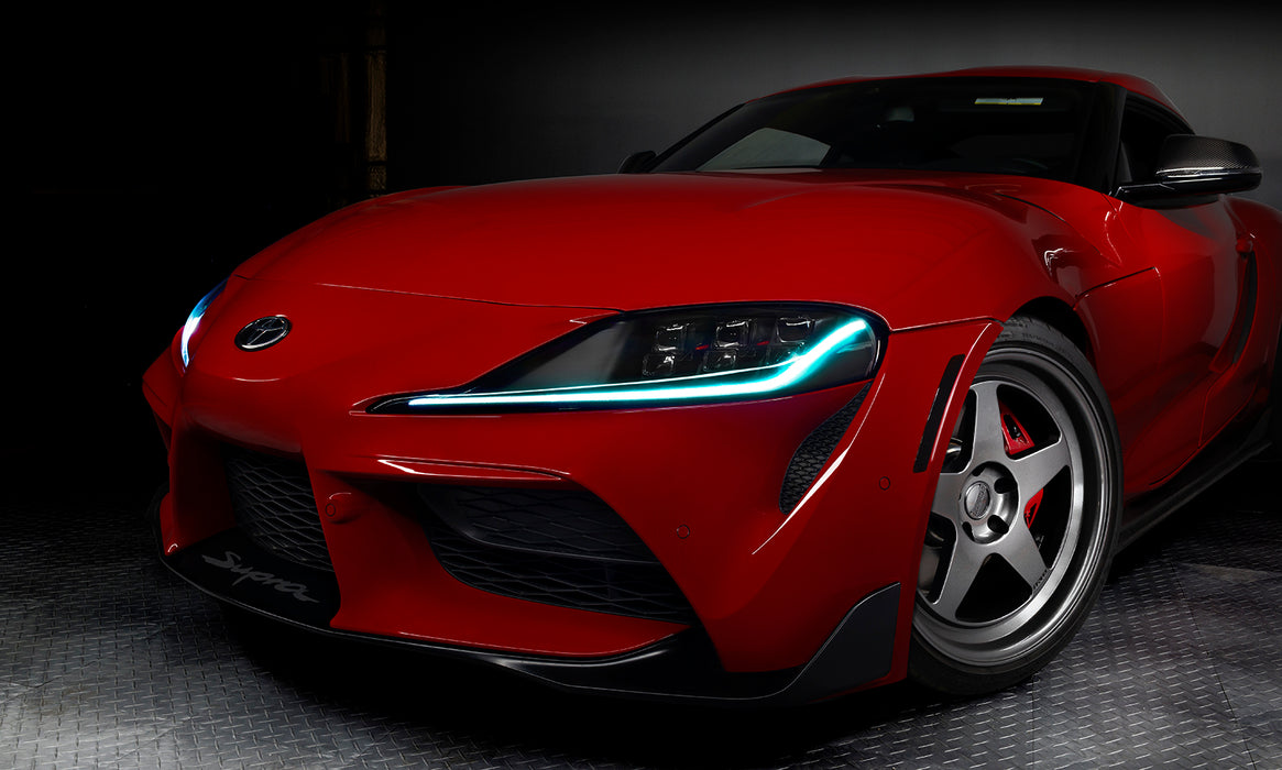 Close-up on the front end of a red Toyota Supra, with cyan headlight DRLs.