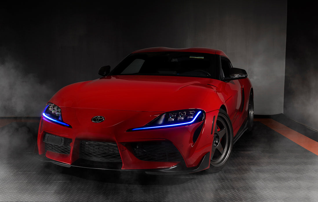 Three quarters view of a red Toyota Supra with blue headlight DRLs.