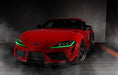 Three quarters view of a red Toyota Supra with green headlight DRLs.