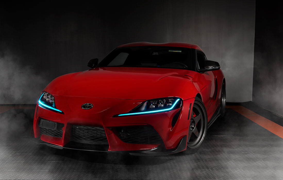 Three quarters view of a red Toyota Supra with cyan headlight DRLs.