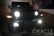 Black Jeep in a garage with very bright headlights and fog lights.