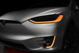 Close-up on the headlights and fog lights of a Tesla Model X with amber DRLs.