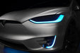 Close-up on the headlights and fog lights of a Tesla Model X with cyan DRLs.