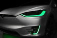 Close-up on the headlights and fog lights of a Tesla Model X with green DRLs.