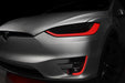 Close-up on the headlights and fog lights of a Tesla Model X with red DRLs.