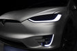Close-up on the headlights and fog lights of a Tesla Model X with white DRLs.