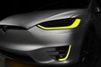 Close-up on the headlights and fog lights of a Tesla Model X with yellow DRLs.